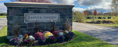 stone sign with the words Keswick Cemetery, grave markers in background and flowers in front