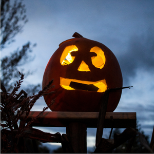 A lit jack-o'-lantern sitting on a wooden post at night, with moody clouds in the dark sky behind it.