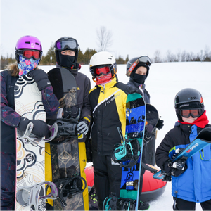 Five kids in winter gear, including coats, mittens, goggles, and balaclavas, with helmets, holding snowboards and skis or standing with an inner tube.