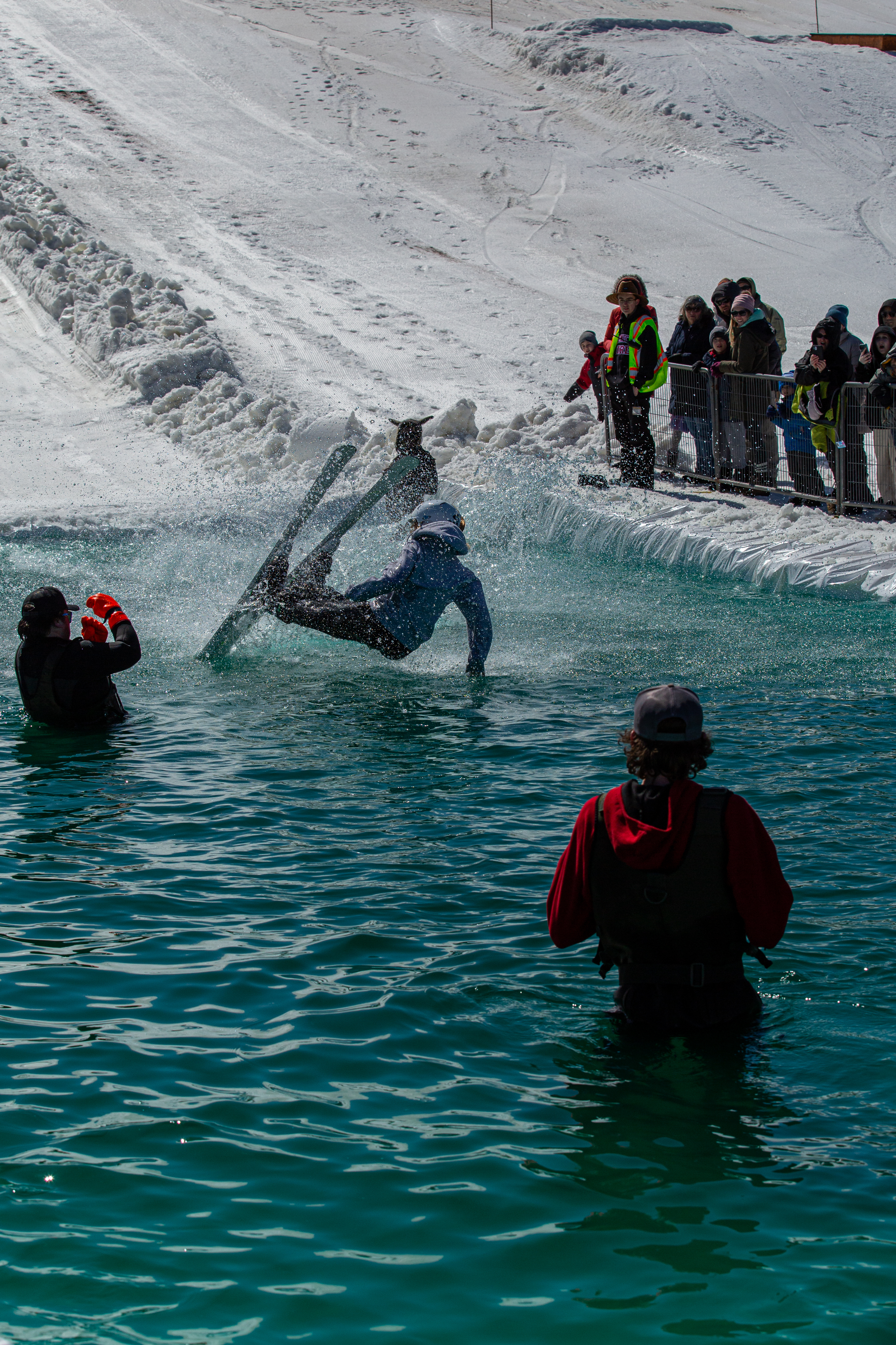 A skier falls backward into the water at the Puddle Jump event, with spectators in the background and staff members standing nearby.