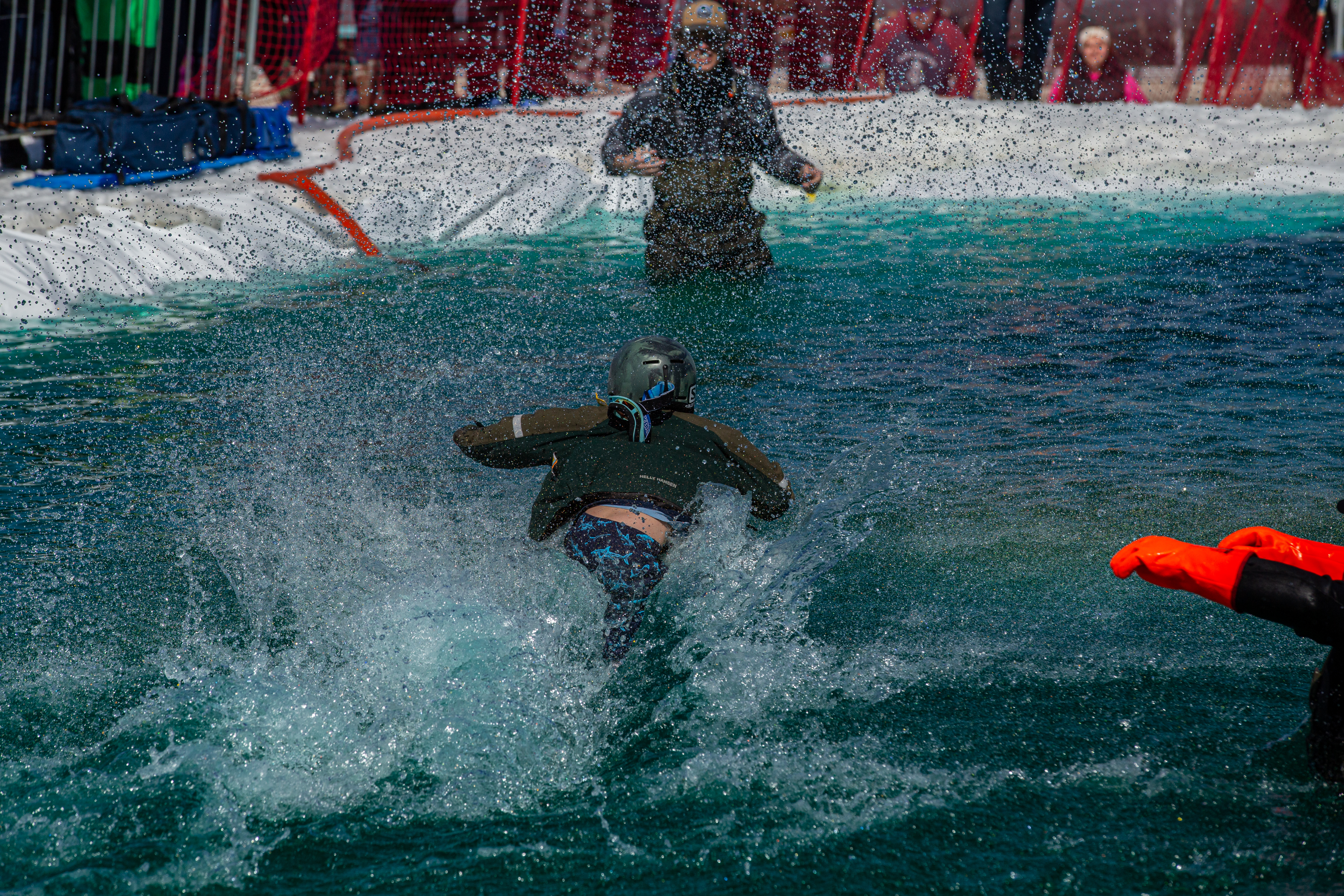 Seen from behind, a child begins to sink into the water with a large splash during the Puddle Jump event, as a staff member stands nearby.