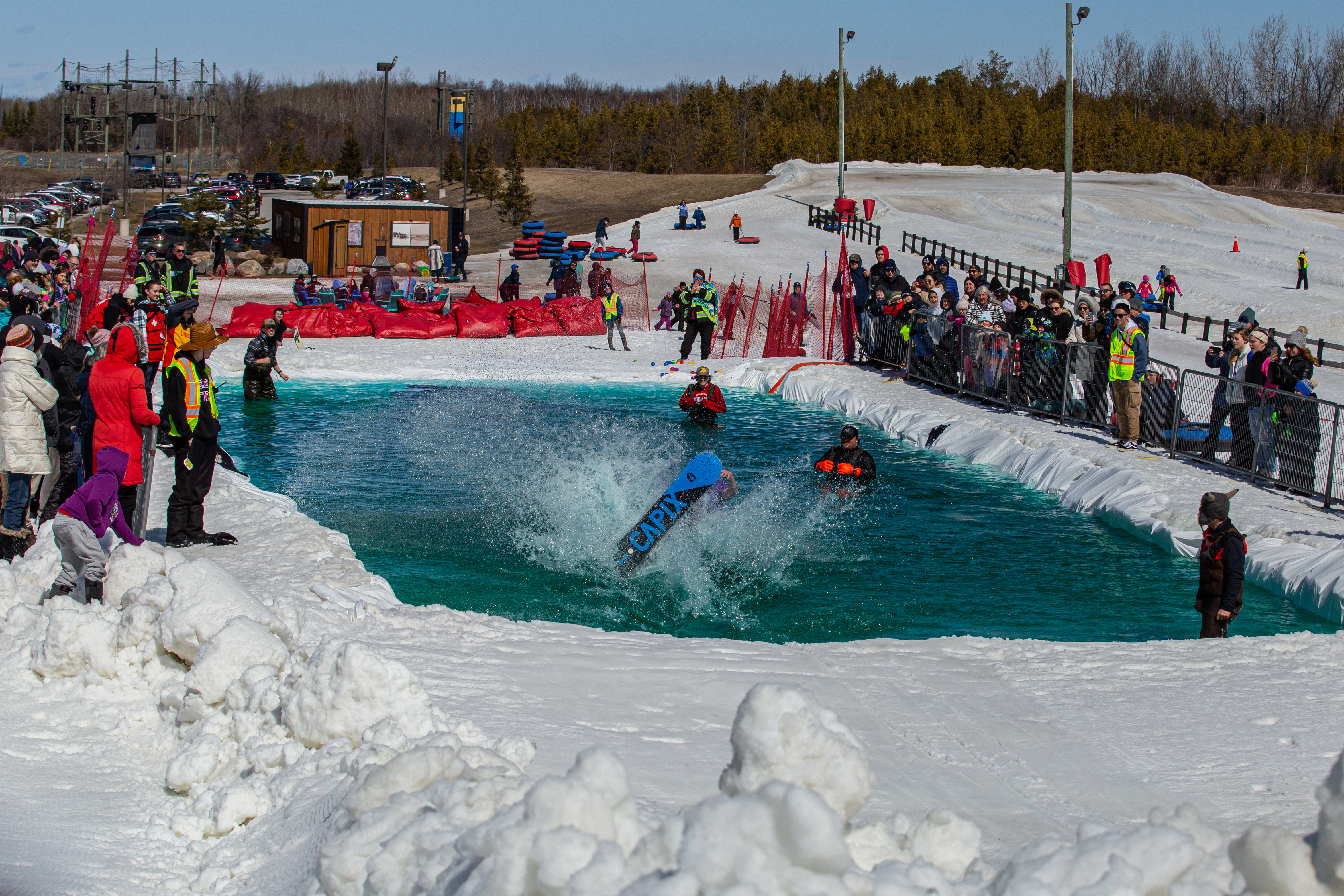 A snowboarder hits the water with a large splash during the Puddle Jump event, as spectators line the snowy hill to watch.