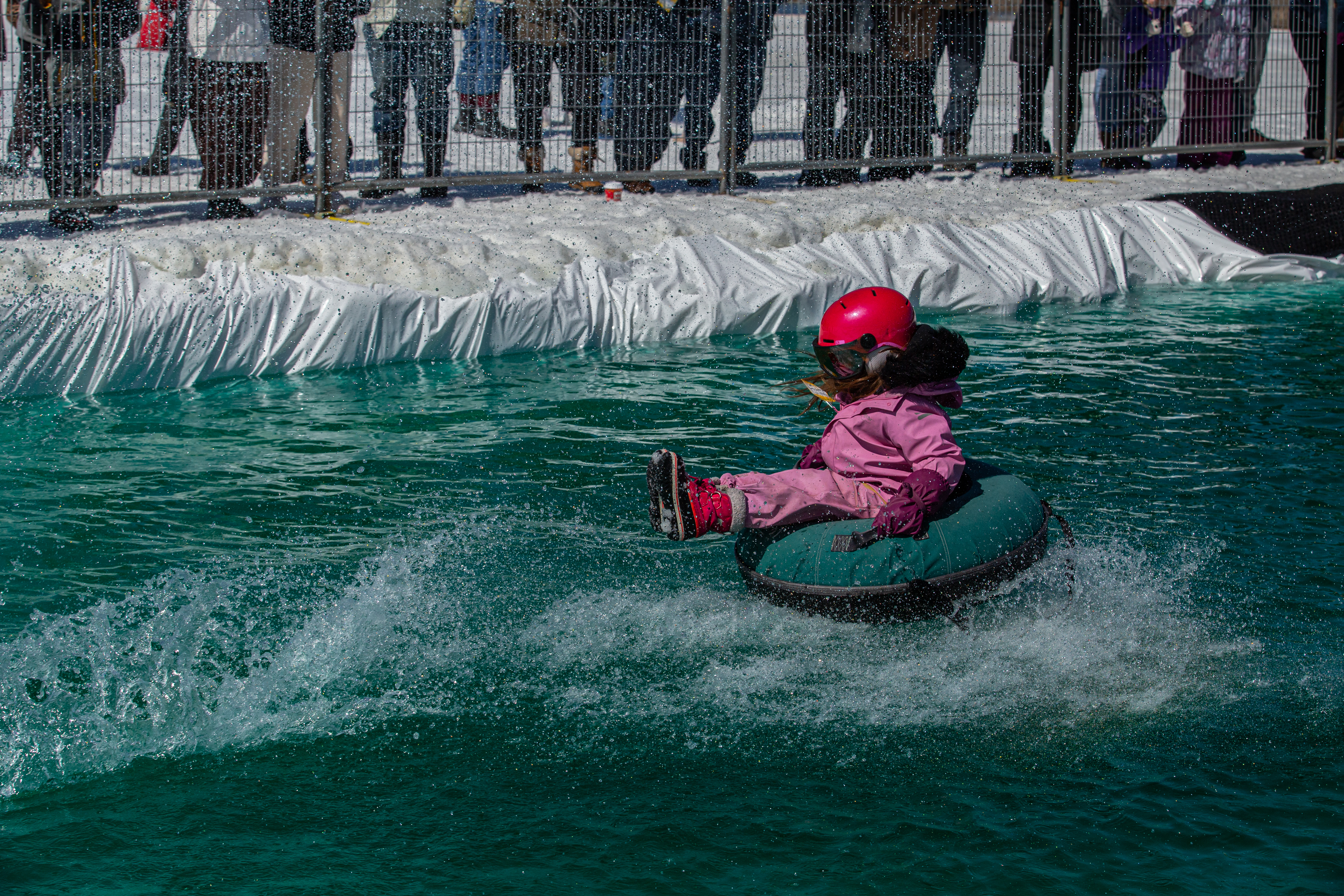 A young girl wearing a helmet rides an inner tube into the water at the Puddle Jump event, creating a small splash