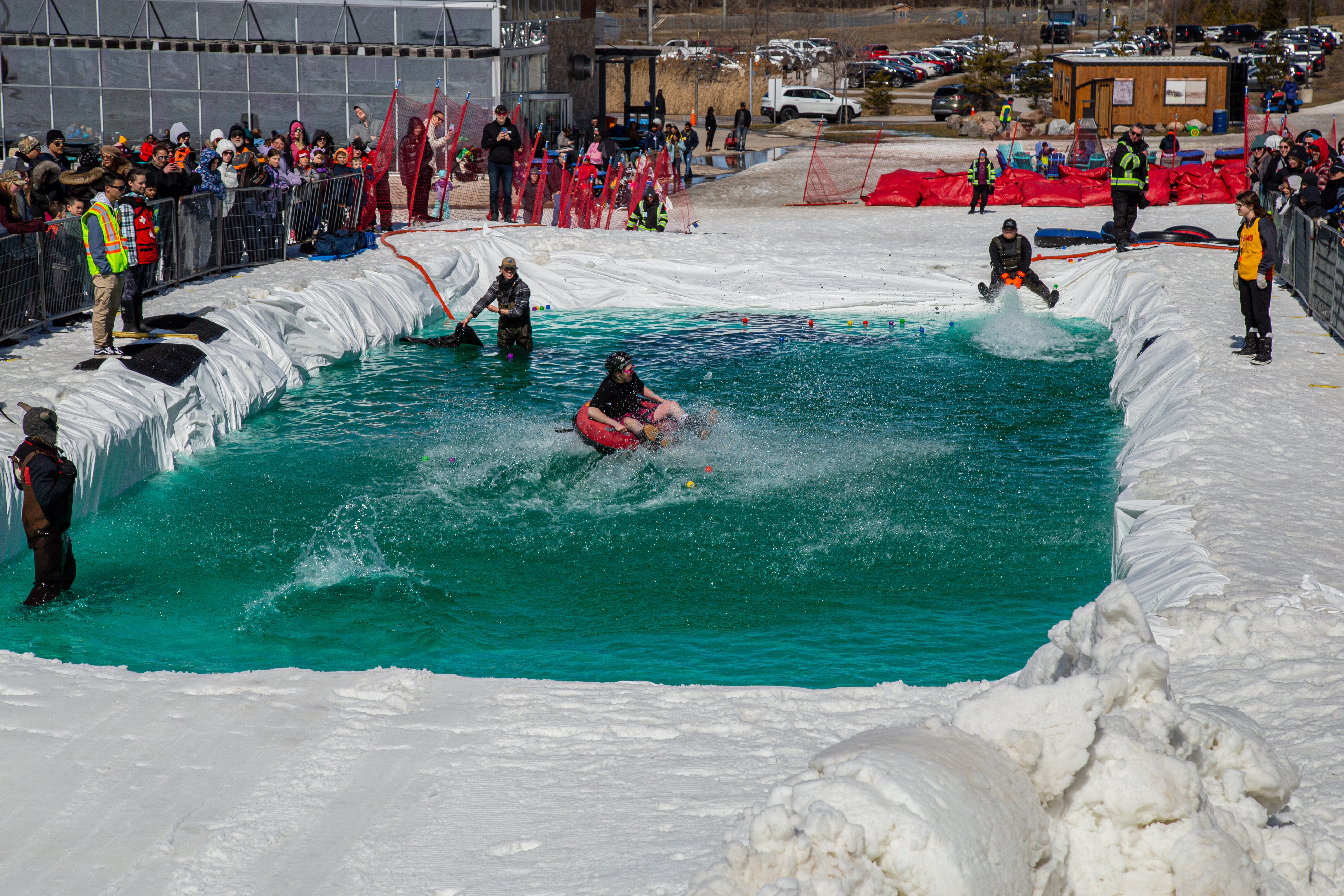 A person on an inflatable tube crashes into the water at the Puddle Jump event, creating a big splash as spectators watch from the snowy hillside