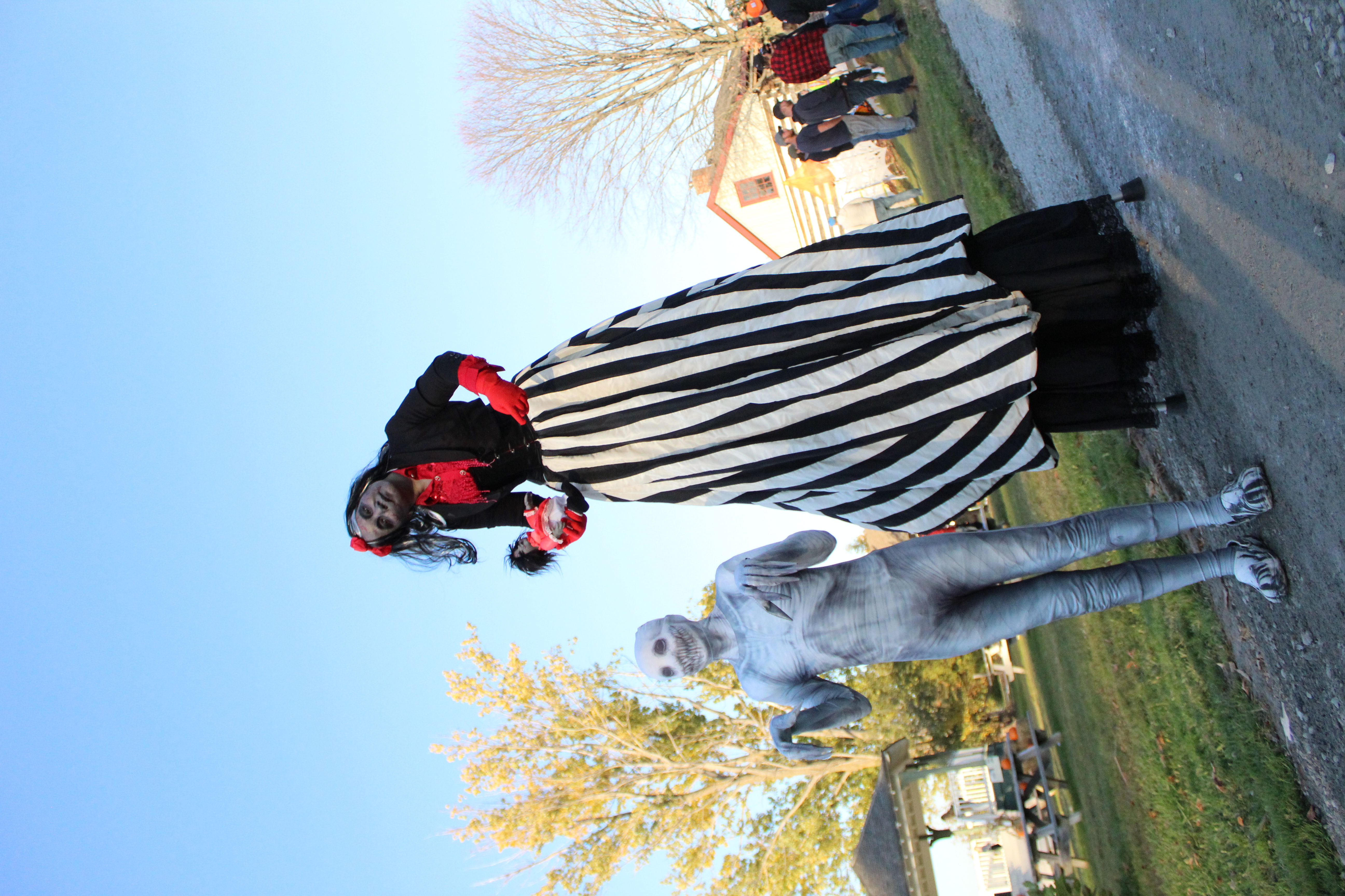 Child dressed in scary halloween costume with another person dressed in scary costume standing on stilts behind