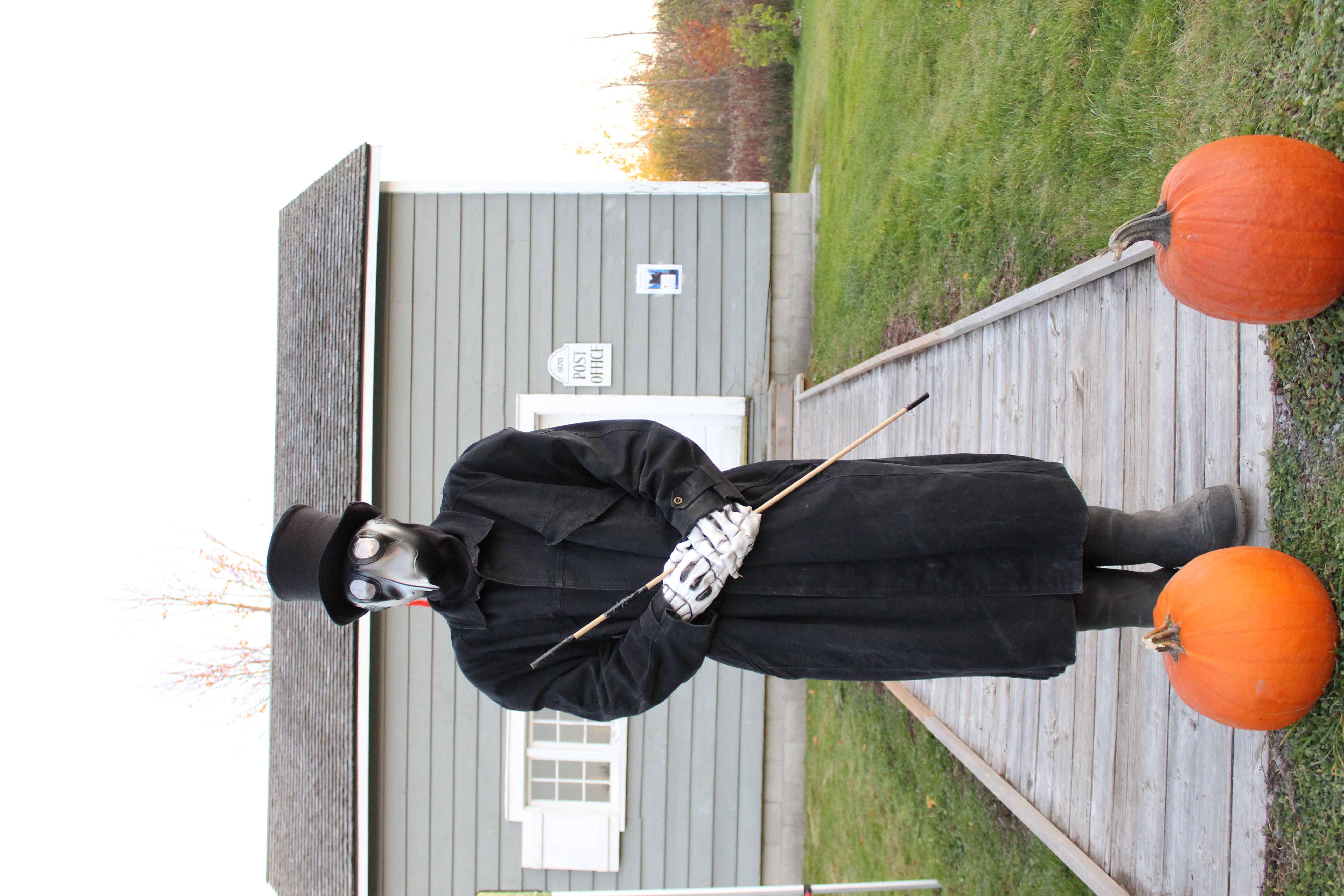Person dressed up as a plague doctor with a mask and long coat standing on boardwalk with pumpkins in front