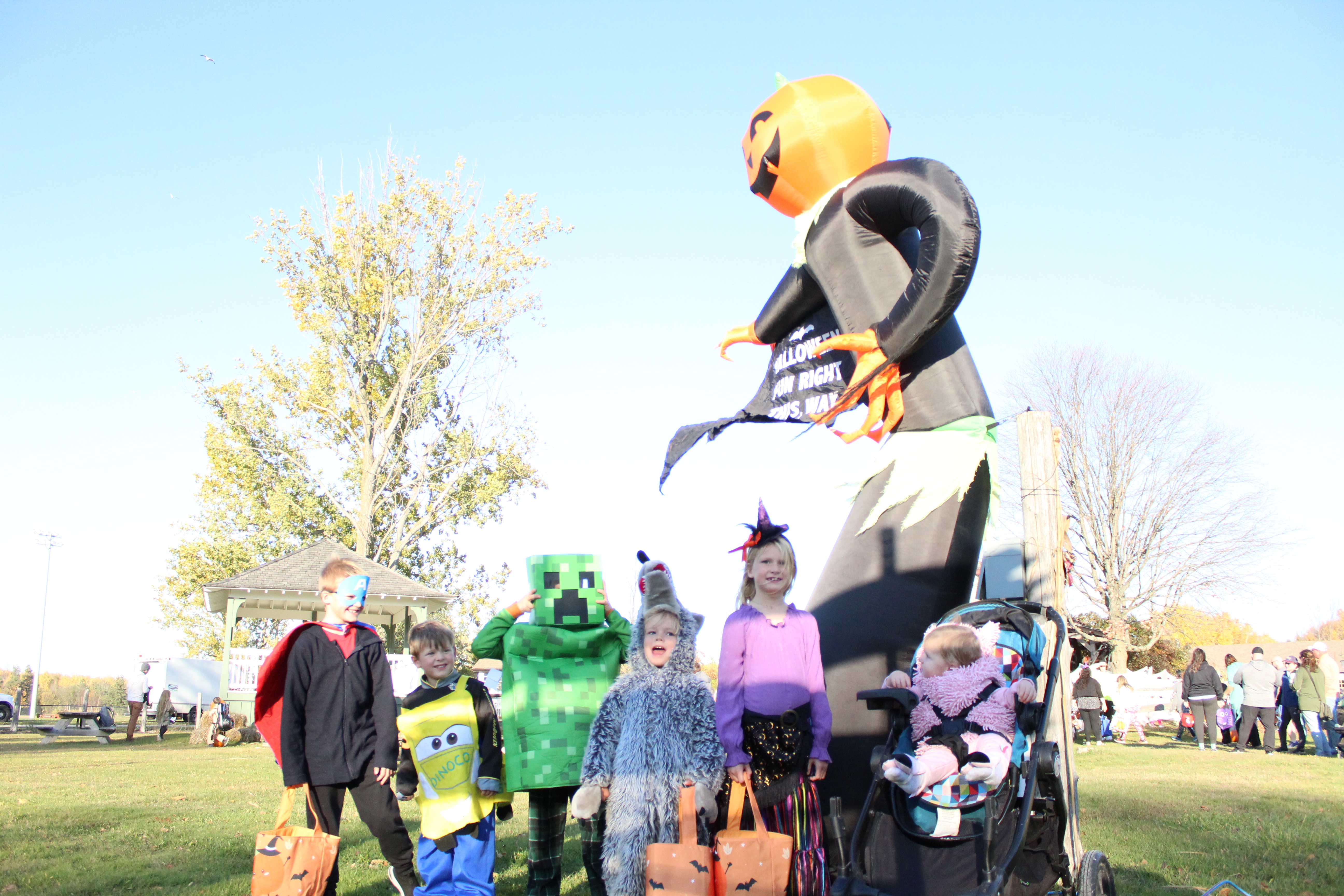 group of children dressed in halloween costumes standing in front of an inflatable decoration man with Jack o lantern head