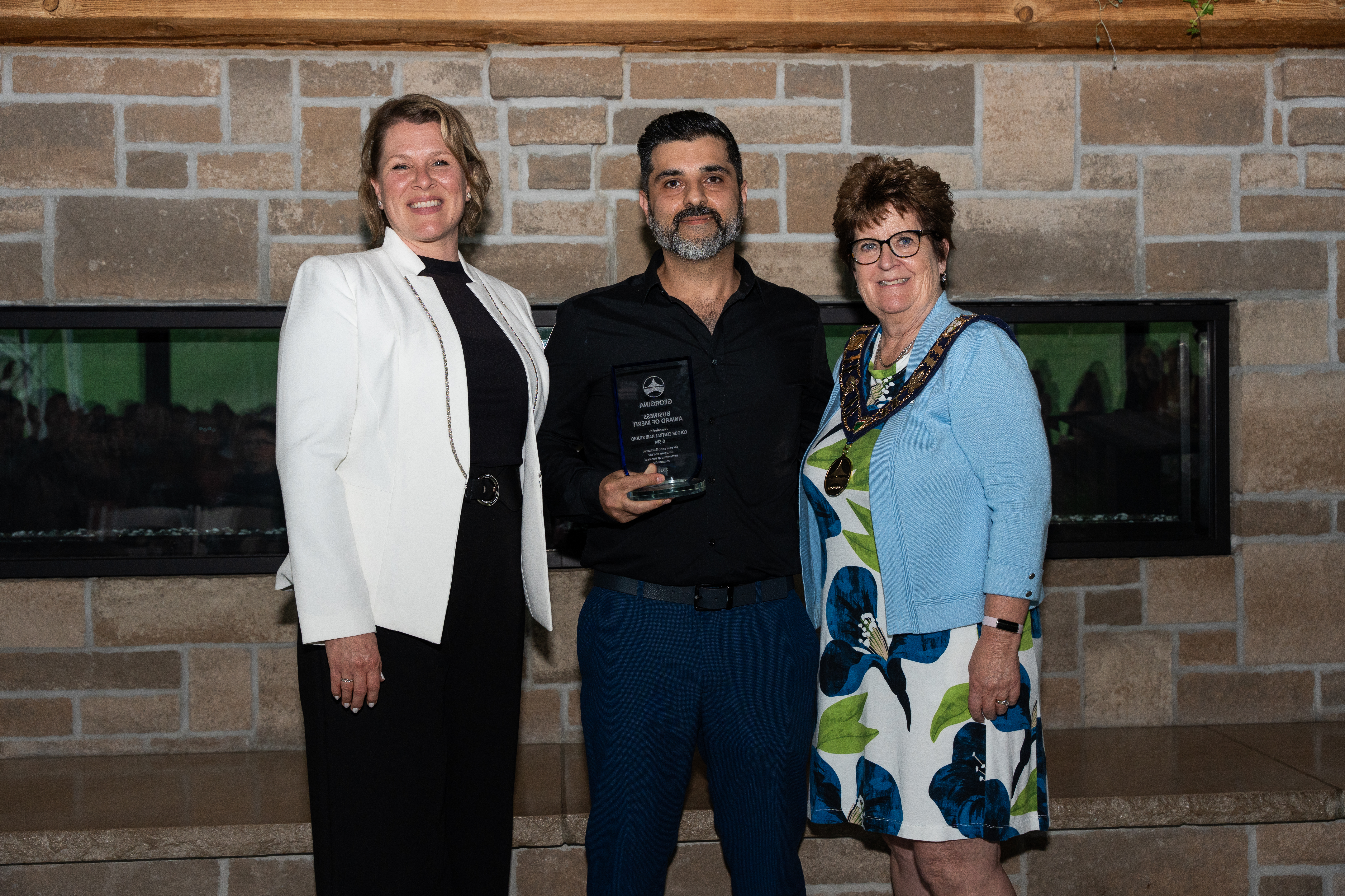 The mayor and Councillor Biggerstaff stand beside an award recipient in front of a brick fireplace, both smiling for the photo.