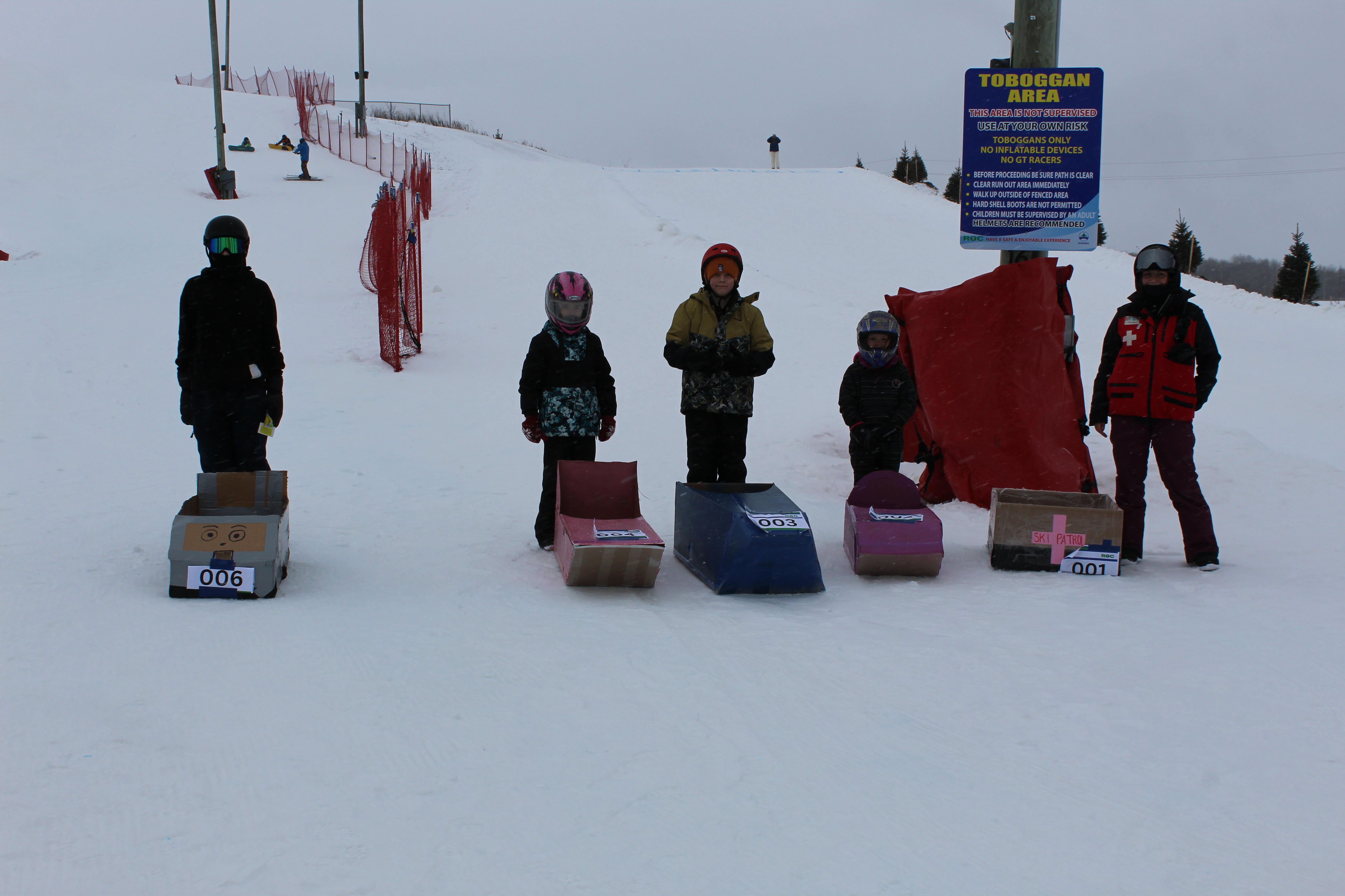 5 kids lined up behind their homemade cardboard toboggans a the start of the race