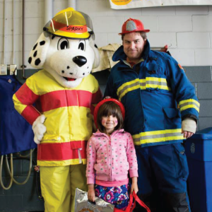 Sparky mascot with child and father who are wearing fake fire helmets
