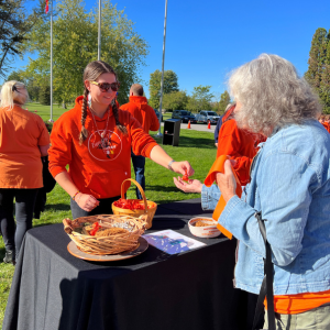 Woman in an orange shirt handing something to an older lady with flagpoles in the background