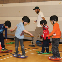 4 children on boards with helmets and a instructor