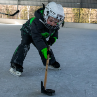 small child with hockey stick and helmet on ice