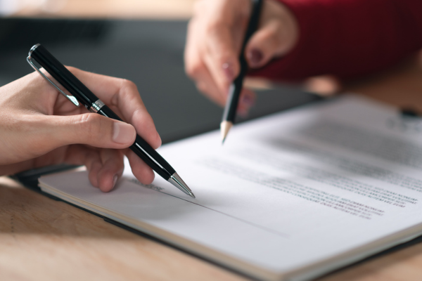 Two hands with pens signing a document