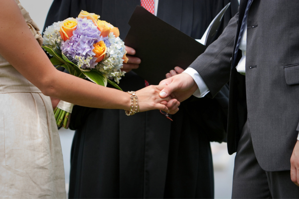 Bride and groom holding hands with officiant in background