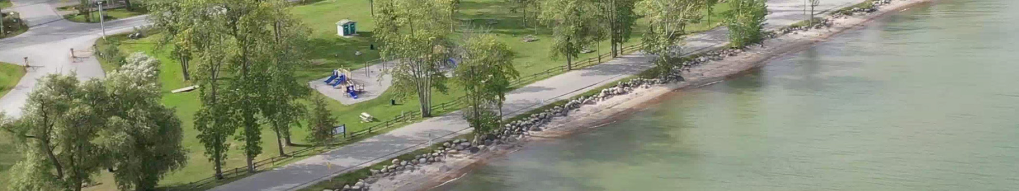 drone photo of a lakeside road and a narrow beach and a park
