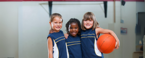 three young children in blue shirts with the child on the right holding a basketball