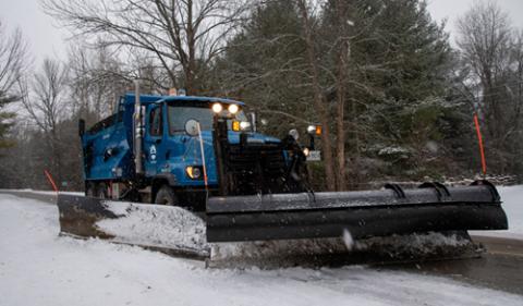 blue snowplow with black front blade clearing snow on the street
