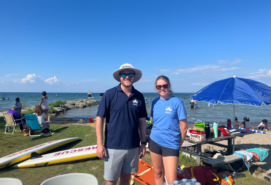 two employees standing at a beach with kayaks and toys behind them