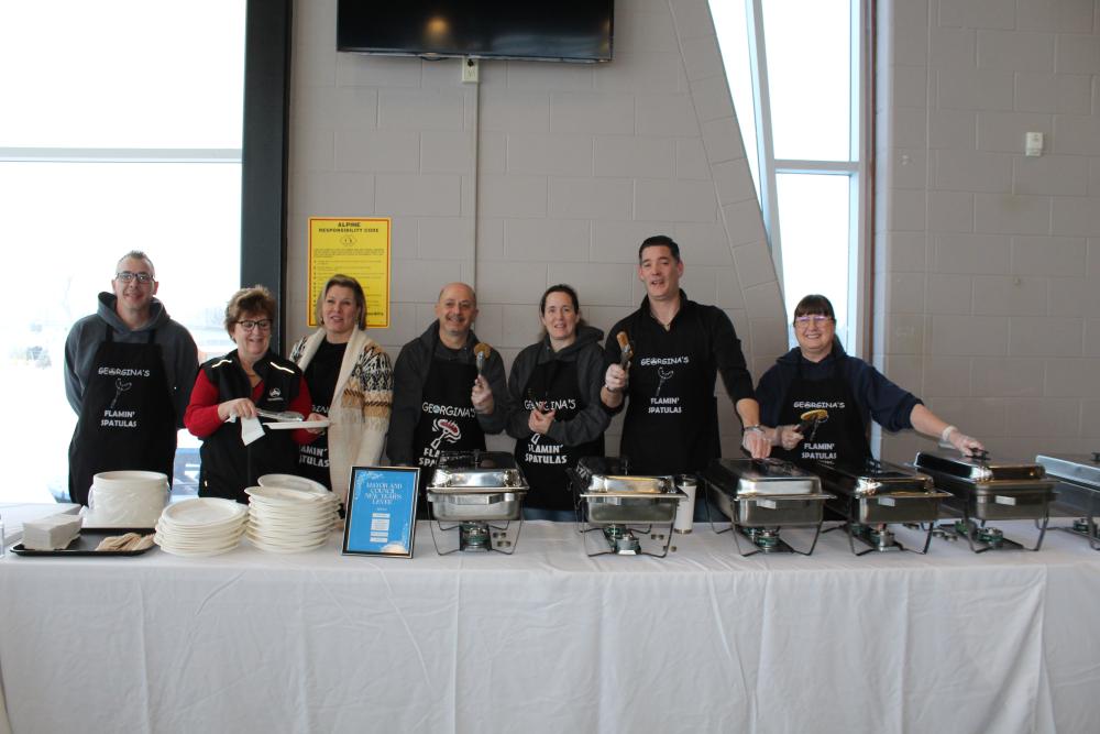 group of people standing behind a table with serving dishes on it
