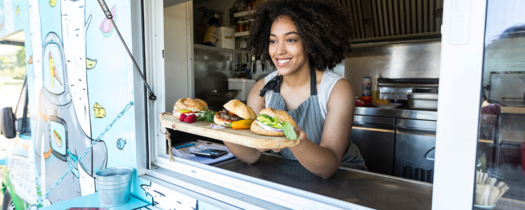 woman holding tray of food out window of food truck