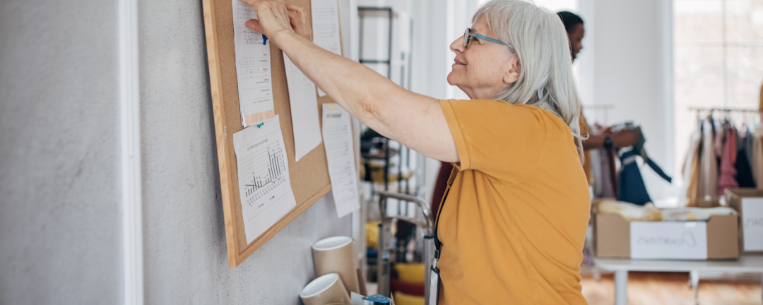 older female pinning a paper to a bulletin board 